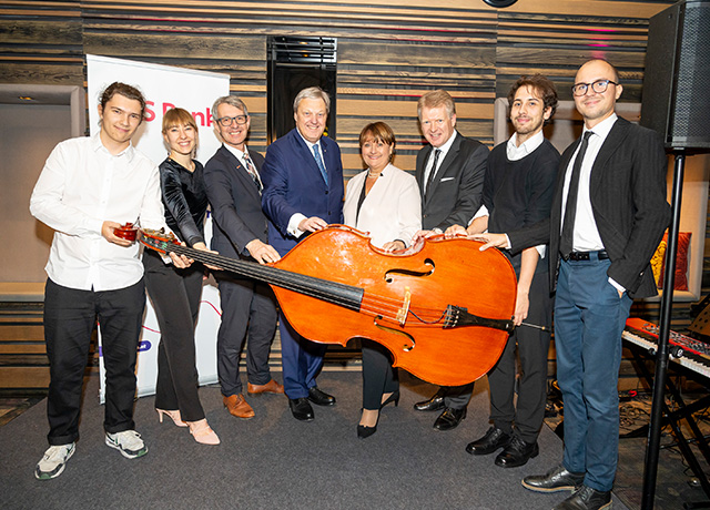 Sieben Personen, darunter Frau Herta Stockbauer und Herr Nikolaus Juhász, halten ein großes Instrument in der Hand.