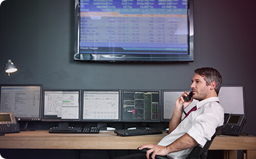 Mann am Telefon vor mehreren Bildschirmen mit Aktiencharts