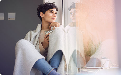 Frau mit Decke schaut aus dem Fenster