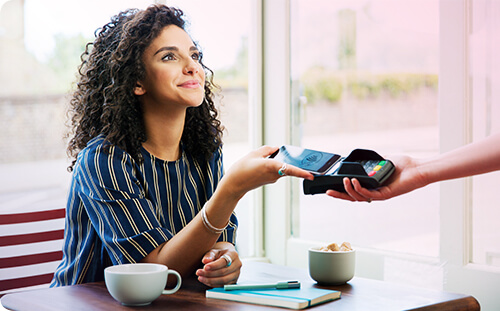 Frau sitzt in Kaffee und bezahlt mit Smartphone