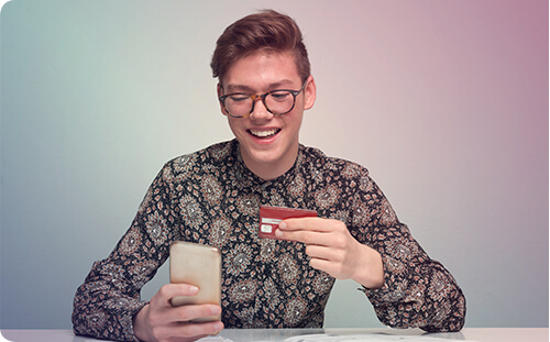 Junger Bub lächelt mit Smartphone und Bankkarte