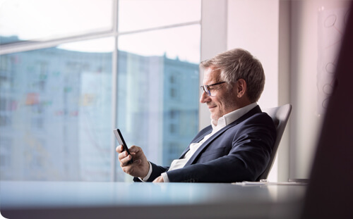 Business Mann sitzt im Büro und benutzt Business App am Handy