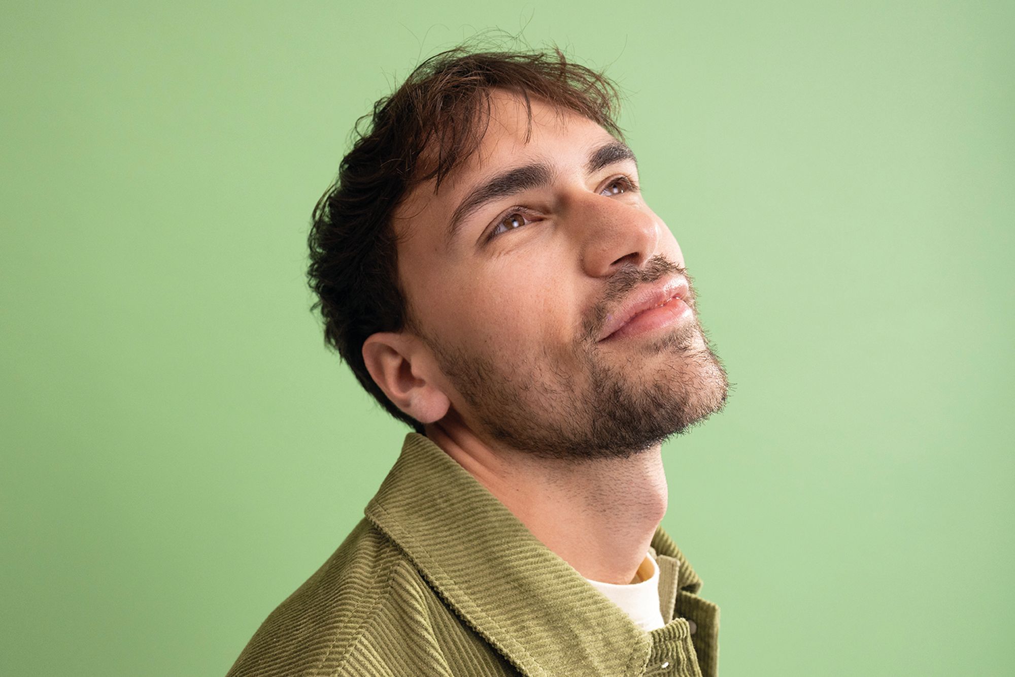 Junger Mann vor grünem Hintergrund mit Blick Richtung Decke.