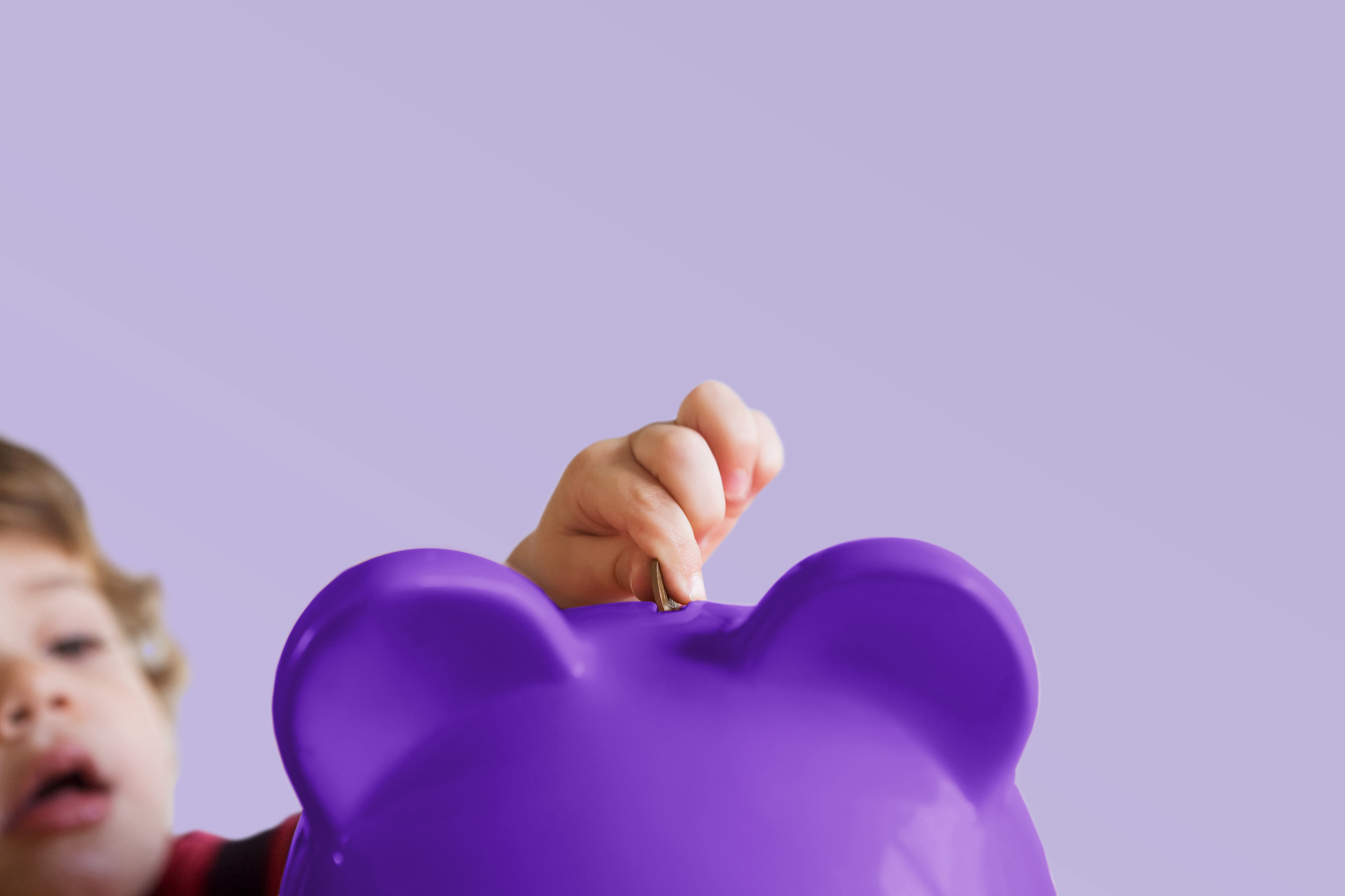 Kind wirft Geld in ein violett abgeschnittenes Sparschwein - Landscape
