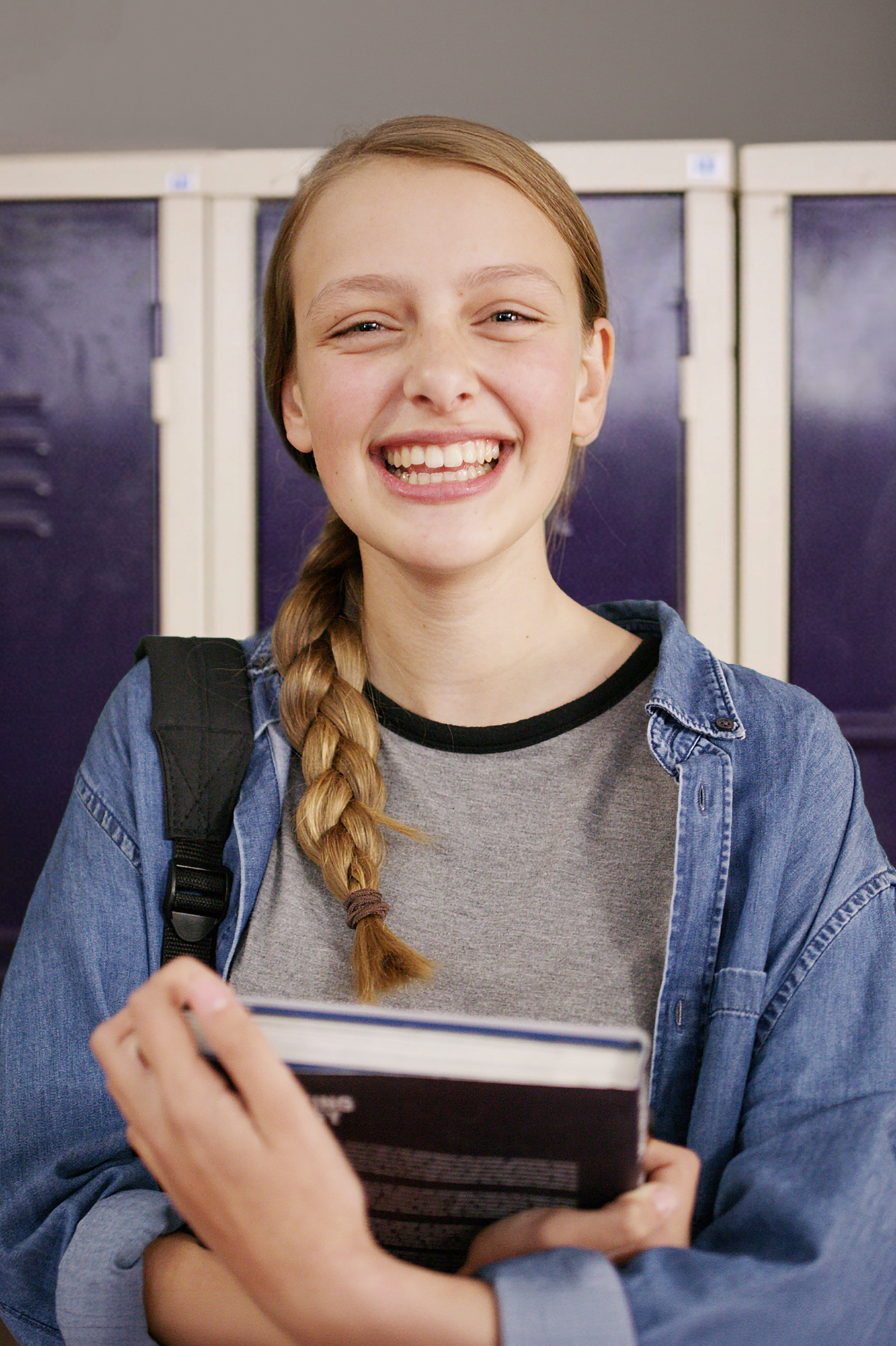 Lächelnde Schülerin im Teenageralter steht vor lila Schulspinden in einem Schulflur. Lächelnde Schülerin im Teenageralter steht vor lila Schulspinden in einem Schulflur.